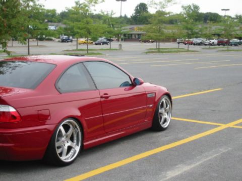 1998 Ford Crown Victoria - A red coupe with custom wheels is parked in a lot, with other vehicles and a building in the background.