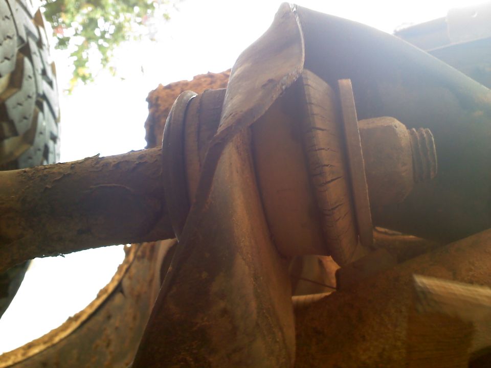 Close-up of a rusted suspension component, possibly a bushing or mount, with a tire visible on the left
