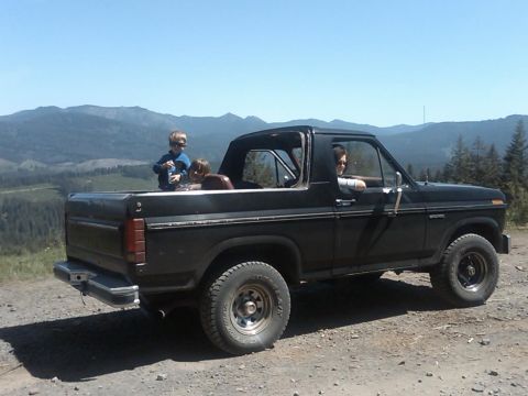 1985 Ford Bronco - A black Ford Bronco is parked on a dirt road with a scenic mountain view, carrying passengers including two children.