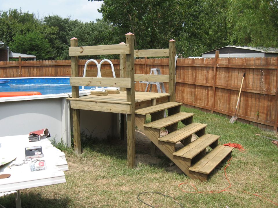 Wooden deck with stairs next to an above-ground pool. Pool ladder is visible on the deck