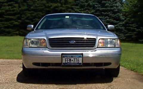 2000 Ford Crown Victoria - A silver 2000 Ford Crown Victoria is parked outside with trees in the background.