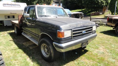 1989 Ford Bronco - This 1987 Ford F-Series truck has a flatbed conversion and is parked outdoors with other vehicles.