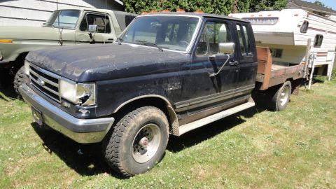 1989 Ford Bronco - A dark blue Ford F-Series flatbed truck is parked next to a green SUV, with a camper in its bed.