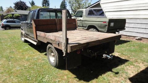 1989 Ford Bronco - A green SUV is parked in a yard next to a flatbed truck.