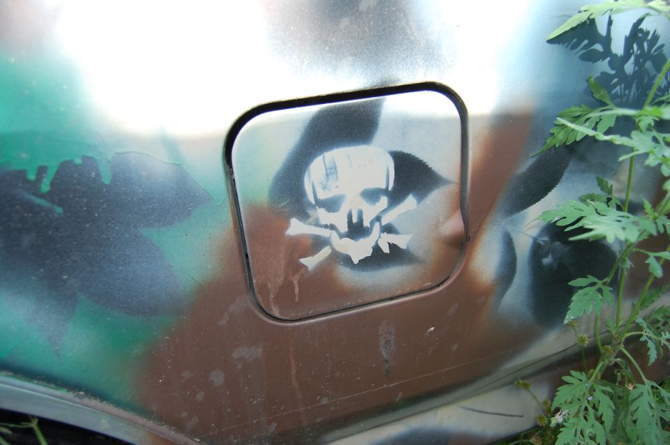 close-up of a vehicle's fuel door with a skull and crossbones sticker, painted in camouflage colors