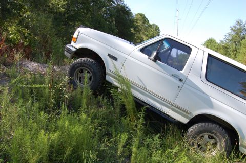 1994 Ford Bronco - White 1994 Ford Bronco navigates a steep, grassy embankment during an off-road excursion.