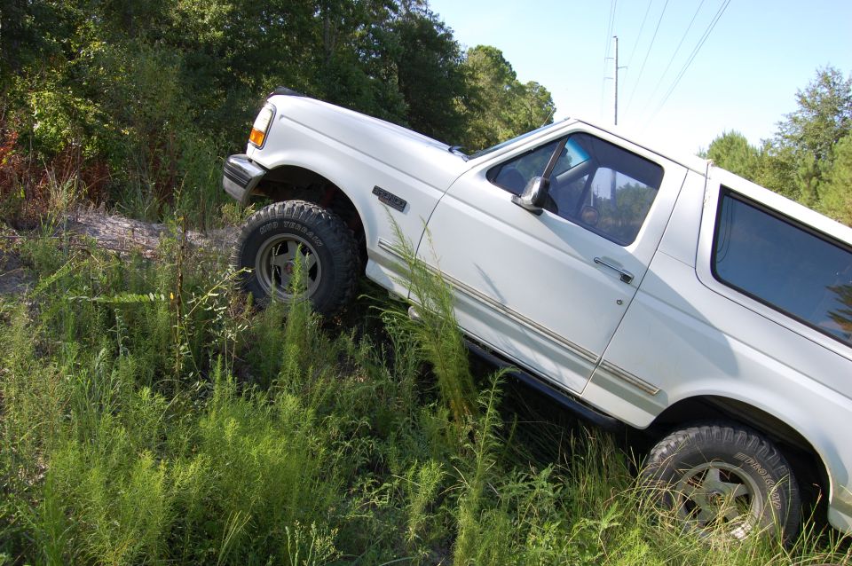 White 1994 Ford Bronco driving off-road on a grassy incline