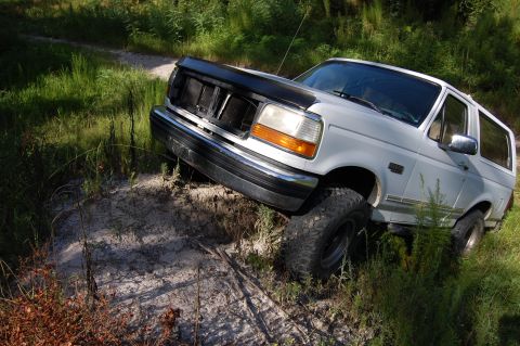 1994 Ford Bronco - White 1994 Ford Bronco navigating an off-road trail with overgrown vegetation.