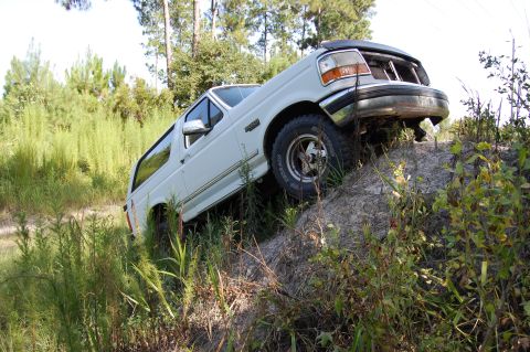 1994 Ford Bronco - A white 1994 Ford Bronco navigates an off-road incline, surrounded by vegetation.
