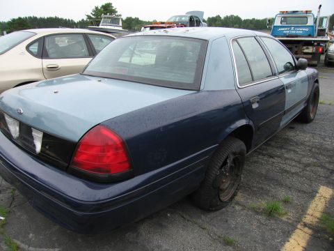 2001 Ford Crown Victoria - A two-tone Ford Crown Victoria is parked in a lot with a tow truck visible in the background.