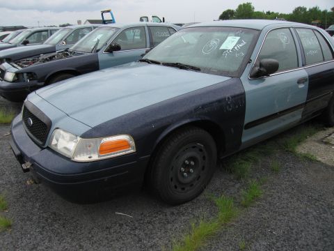 2001 Ford Crown Victoria - Two-tone 2001 Ford Crown Victoria in a vehicle lot, with other cars visible in the background.