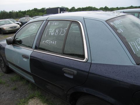 2001 Ford Crown Victoria - A two-tone sedan sits in a lot with chalk markings on its windows, including a year '03'.