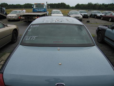 2001 Ford Crown Victoria - Blue sedan in a lot with other vehicles and a tow truck. White markings on rear window.