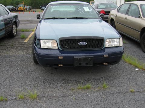 2001 Ford Crown Victoria - A two-tone Ford Crown Victoria sits in a lot with other vehicles. The front passenger side headlight is missing.