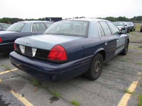 2001 Ford Crown Victoria - A two-tone 2001 Ford Crown Victoria is parked in a lot with other vehicles.