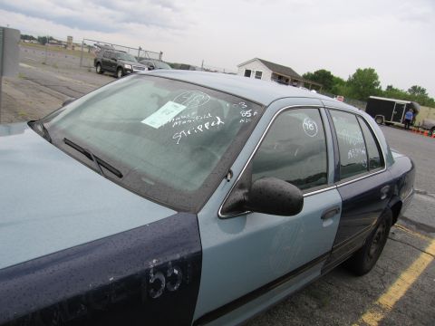 2001 Ford Crown Victoria - A two-tone sedan, possibly a 2001 Ford Crown Victoria, is shown from a three-quarter front angle with visible markings on its windows.