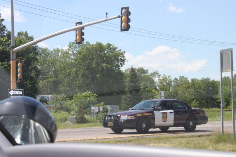 2003 Ford Crown Victoria - A 2003 Ford Crown Victoria, marked as a State Trooper vehicle, drives on a road under a traffic light.