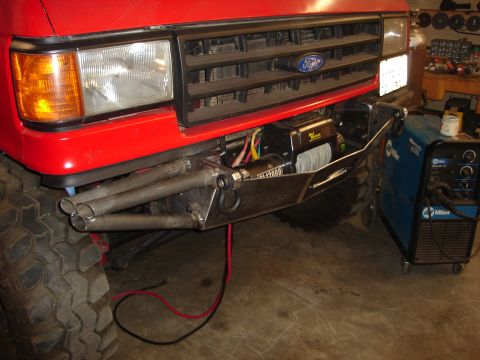 1989 Ford Bronco - Custom bumper with winch installed on a red Ford Bronco, with welding equipment in the background.