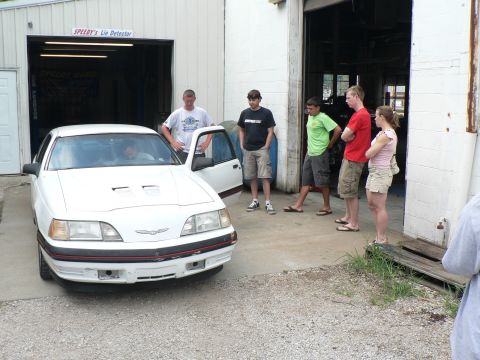 2004 Mercury Marauder - A white sedan with a red stripe and hood scoops is parked outside a garage with several people standing nearby.