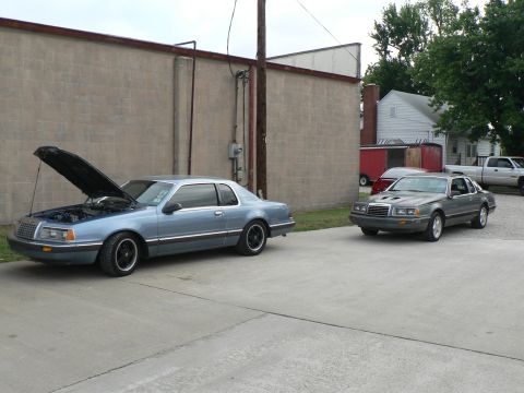 2004 Mercury Marauder - Two Ford Thunderbirds are parked outside a building, one with its hood up.