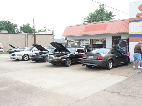 2004 Mercury Marauder - Multiple vehicles are parked in front of a building with various signs, some hoods are open.