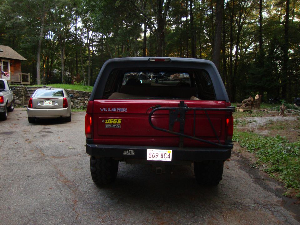 Red Ford Bronco, rear view, with spare tire carrier and JEGS sticker. Another car is parked behind it
