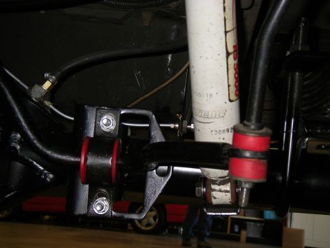 1990 Ford Bronco - Close-up view of the suspension system, red bushings and a Rancho shock absorber, with another vehicle partially visible.