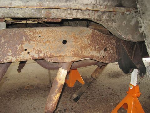 1979 Ford Bronco - The heavily rusted frame and suspension components of a vehicle are visible, supported by jack stands.