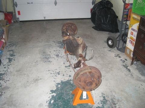 1979 Ford Bronco - A rusty rear axle assembly is supported by an orange jack stand in a garage setting.