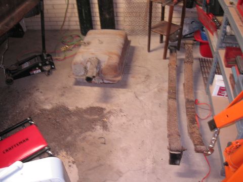 1979 Ford Bronco - A rusty fuel tank and leaf springs are visible on a garage floor next to a jack and a red stool.