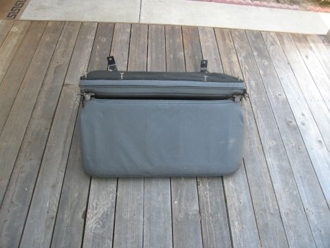 1986 Ford Bronco - A folding seat with fabric upholstery is shown resting on a weathered wooden surface.