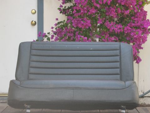 1986 Ford Bronco - A gray car seat with horizontal stitching is shown in front of a door and flowering bush.