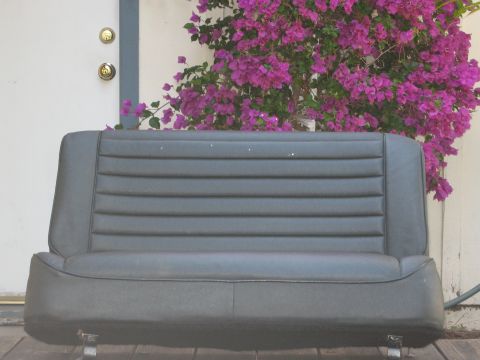 1986 Ford Bronco - Gray car seat with horizontal stitching, photographed outdoors in front of a door and flowering bush.