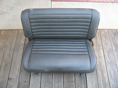 1986 Ford Bronco - A black vinyl car seat with horizontal pleats is shown from the front, resting on wooden planks.