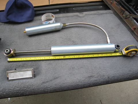 1986 Ford Bronco - Two Pro Comp shocks are laid out on a gray surface with a measuring tape and a blue cap nearby.
