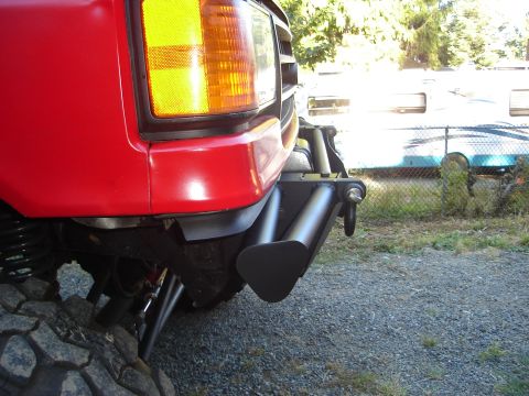 1989 Ford Bronco - Close-up of a red vehicle's front corner, showing a custom bumper and large tires.
