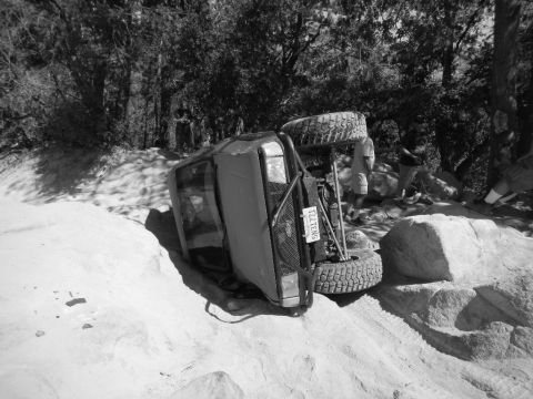 1997 Ford Ranger - An off-road vehicle has rolled onto its side in a rocky, sandy environment with onlookers present.