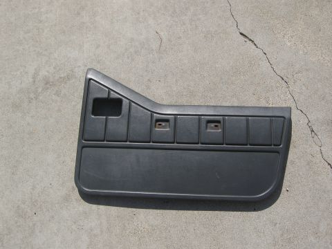 1986 Ford Bronco - This dark gray plastic door panel features a series of rectangular indentations and a larger pocket at the bottom.