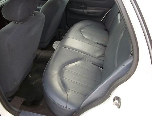 Back seat of a car, showing dark gray upholstery and floor mats. A Supermotors.net logo is in the corner