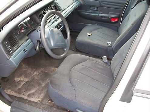 Interior of a light-colored sedan, showing the dashboard, steering wheel, and front seats. The car appears worn