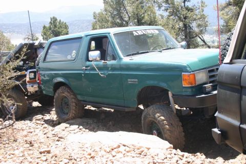 1991 Ford Bronco - A green Ford Bronco navigates a rocky trail, with another vehicle partially visible to the right.