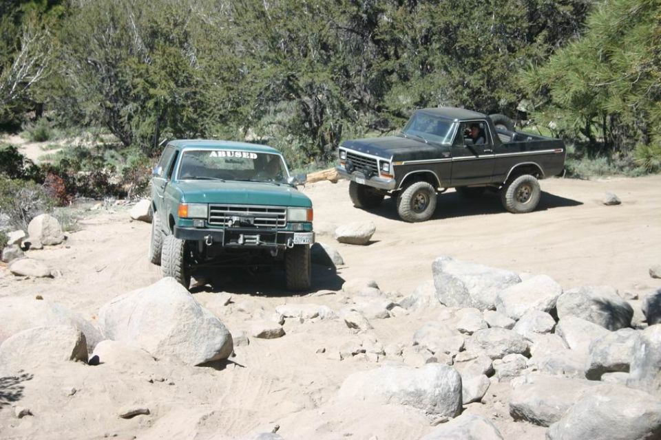 Two SUVs parked on a dirt road with trees in the background