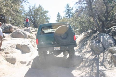 1991 Ford Bronco - A 1991 Ford Bronco navigates a challenging rocky trail, kicking up dust.