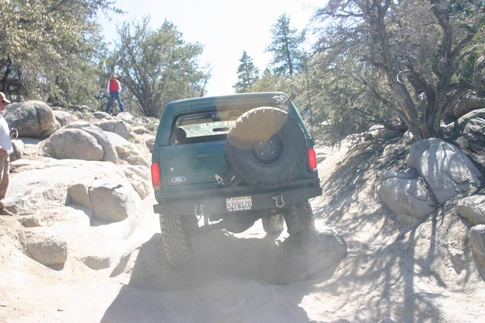 Green 1991 Ford Bronco on rocky terrain, rear view, spare tire mounted externally