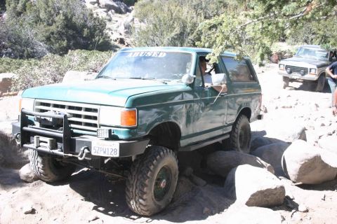 1991 Ford Bronco - A green Ford Bronco tackles a rocky trail, with another vehicle visible behind it.