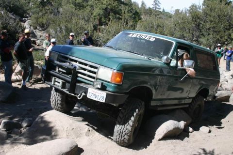 1991 Ford Bronco - This green Ford Bronco is tackling a rocky trail, with onlookers watching its progress.