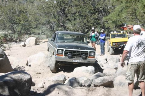 1991 Ford Bronco - A dark green Ford F-Series truck is seen on a rocky off-road trail with other vehicles and people present.