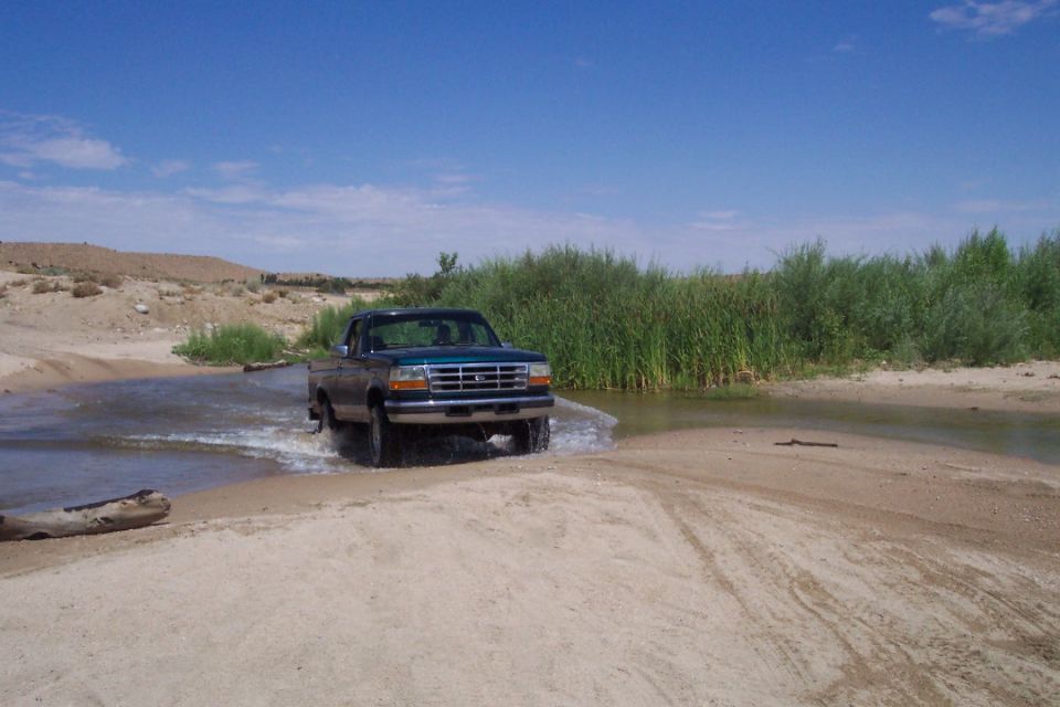 Green 1995 Ford F-150 driving through shallow water
