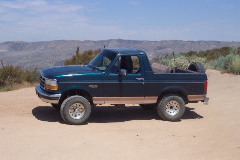 1995 Ford Bronco - Side view of a 1995 Ford Bronco parked on a dirt road in a hilly, arid landscape.