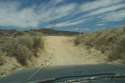 1995 Ford Bronco - View from inside a vehicle on a dusty, off-road path with desert vegetation and utility towers.